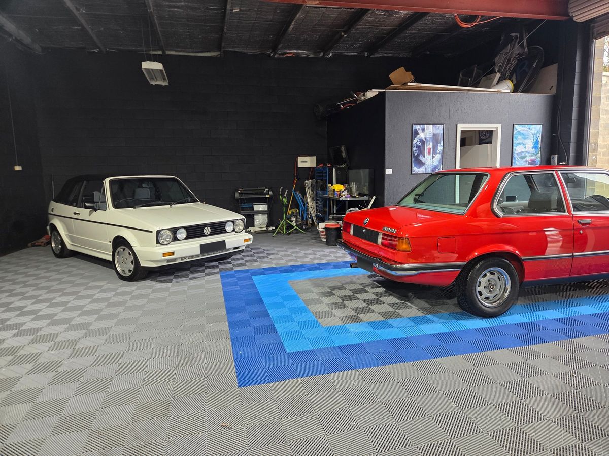 Inside the REVIVD studio in Pambula: a white VW Golf cabriolet and a red BMW E30 on a grey and blue tiled floor